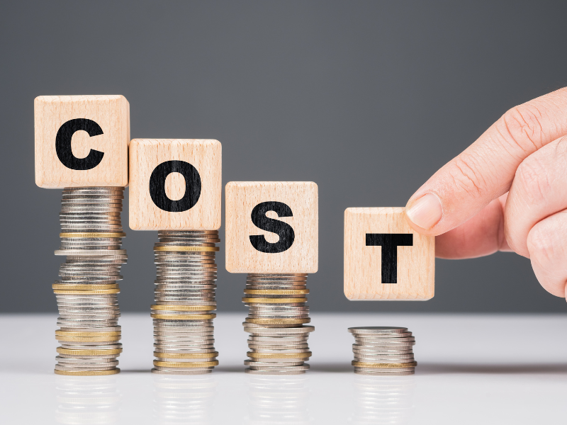 Wooden blocks spelling "COST" stacked on piles of coins