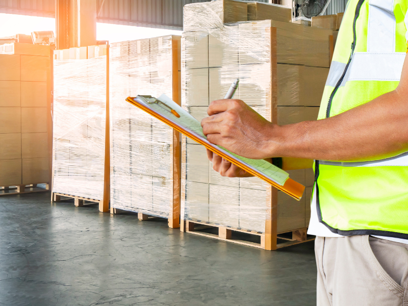 Worker in safety vest checking inventory list in warehouse setting