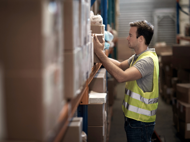 Worker in safety vest arranging stock on warehouse storage shelves
