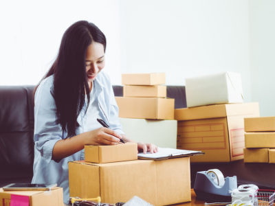 Young woman smiling while writing on boxes, preparing shipments for fulfillment logistics operations
