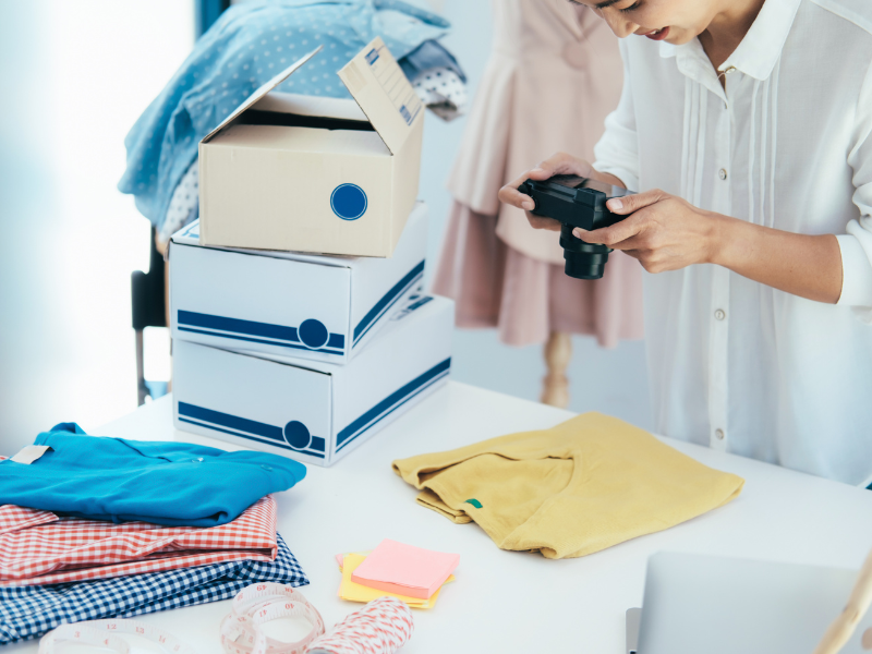 A person photographs clothes near stacked boxes while preparing items for an unboxing session