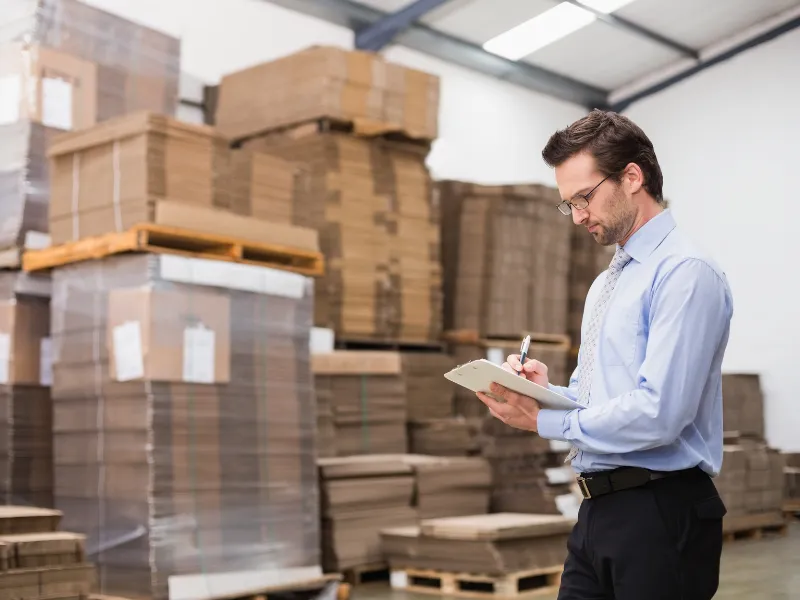 Man in warehouse checking inventory levels on clipboard to manage vendor supply efficiently