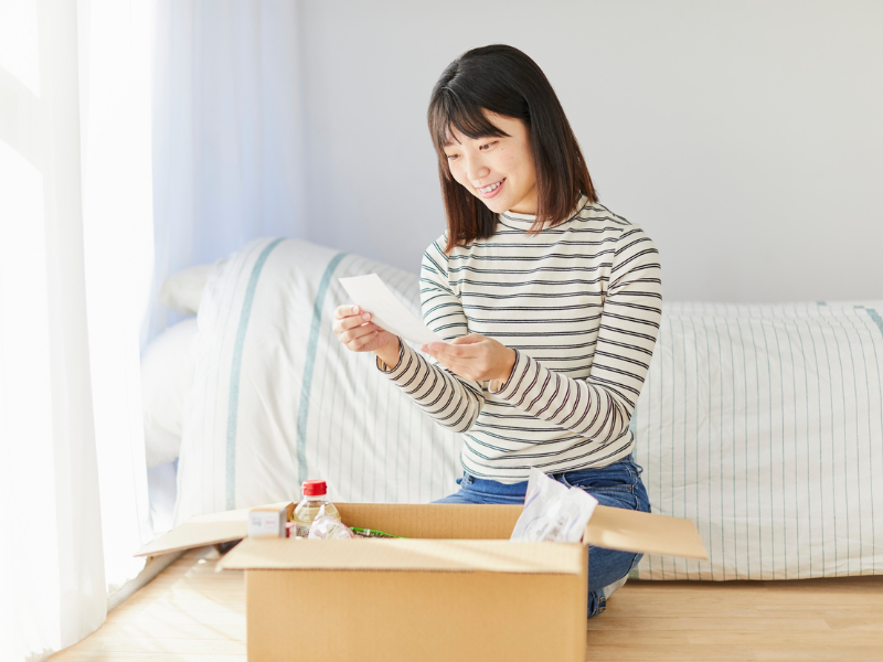 A woman smiles while reading a note from a box of carefully packaged delivery items