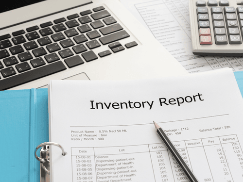 Printed inventory report with charts, pen, and laptop used for tracking warehouse stock levels