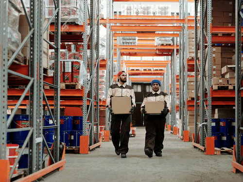 Two workers carry packages in a 3PL facility, ensuring timely warehouse-to-door logistics operations